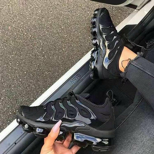 A stylish all-black athletic sneaker featuring a glossy wave-patterned upper and a black transparent air-cushioned sole