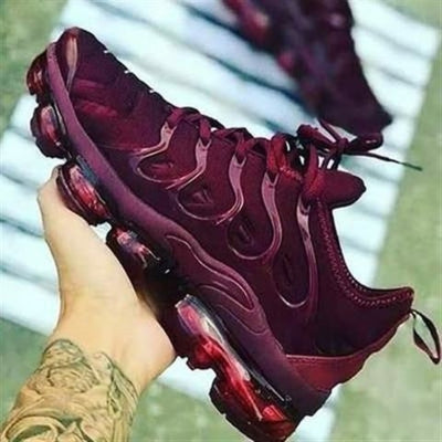 A sleek burgundy athletic sneaker with a wave-patterned upper and a transparent burgundy air-cushioned sole.