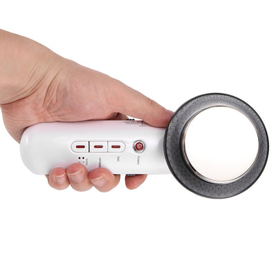 A hand holding a white infrared EMS slimming massager device with a large round metal head surrounded by a black ring
